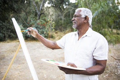 An attractive senior African American man painting on a canvas with acrylic paint.